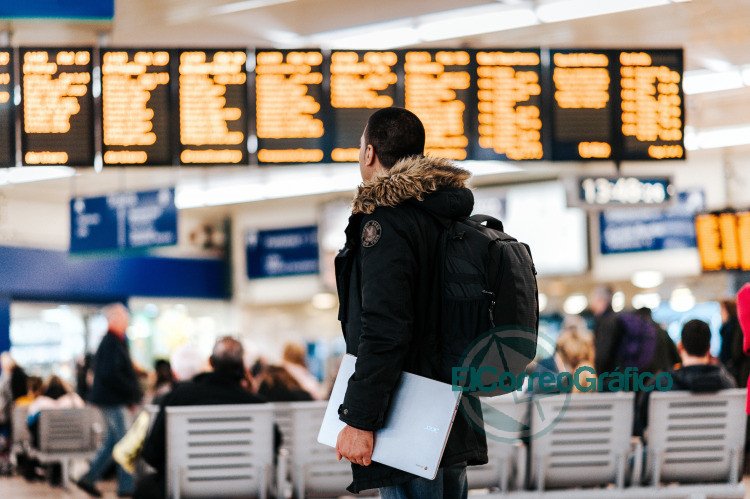man standing inside airport looking at LED flight schedule bulletin board