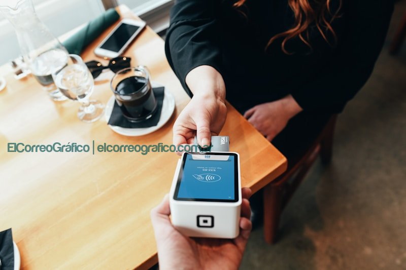 person holding credit card swipe machineTarjeta de Débito: Controla tus gastos y simplifica tus transacciones